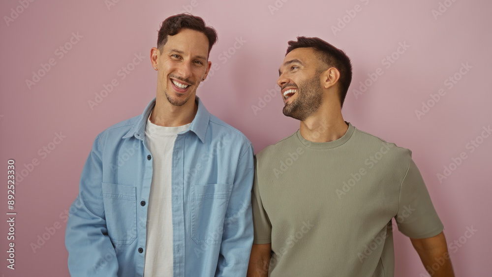 Two men, a couple, smiling and sharing a joyful moment together against a pink background, representing love and family in the lgbtq community. Two men, a couple, smiling and sharing a joyful moment together against a pink background, representing love and family in the lgbtq community.