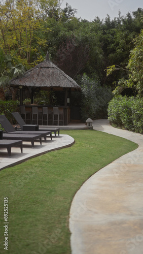 Outdoor tropical cabana with sunbeds at a luxury resort surrounded by lush foliage and a curved path.