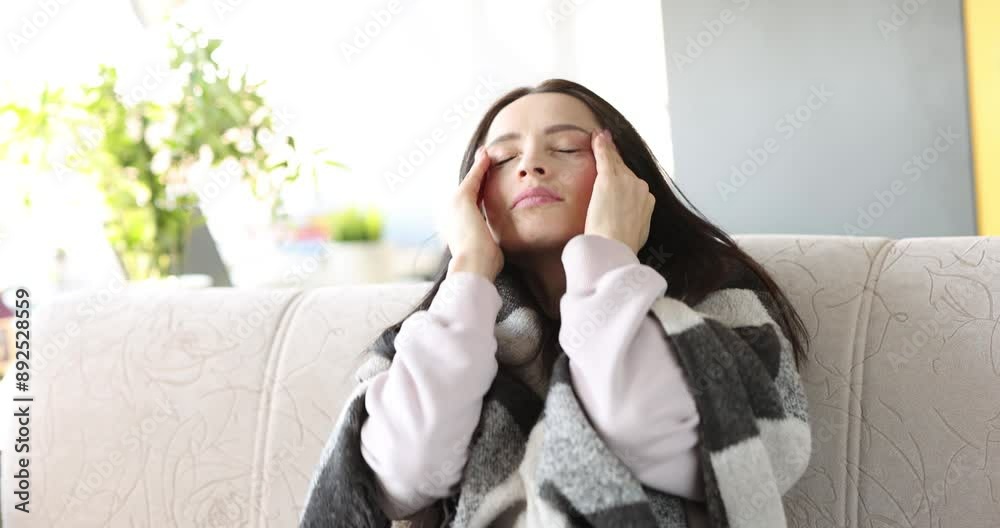 Young woman with severe headache sits on couch. Pain in temple area concept Young woman with severe headache sits on couch. Pain in temple area concept