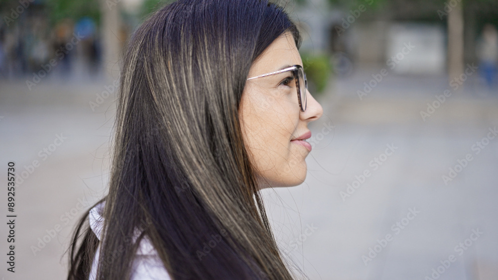 Young beautiful hispanic woman wearing glasses smiling happy looking to the side in the streets of Madrid