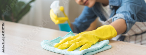 Fotografia Cleanliness asian young woman working chore cleaning on table at home, hand wearing glove using rag rub remove dust with spray bottle