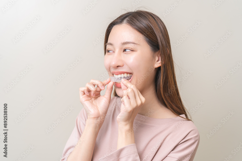 Dental invisible braces, beautiful smiling asian young woman holding invisalign braces, wearing orthodontic silicone trainer, white smile using invisible whitening tray. Stomatology, dental healthcare Dental invisible braces, beautiful smiling asian young woman holding invisalign braces, wearing orthodontic silicone trainer, white smile using invisible whitening tray. Stomatology, dental healthcare
