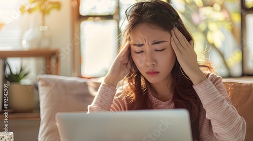 A young Asian woman in front of a laptop closed her eyes and holds her hands behind her temples from overwork and headache. The concept of time management