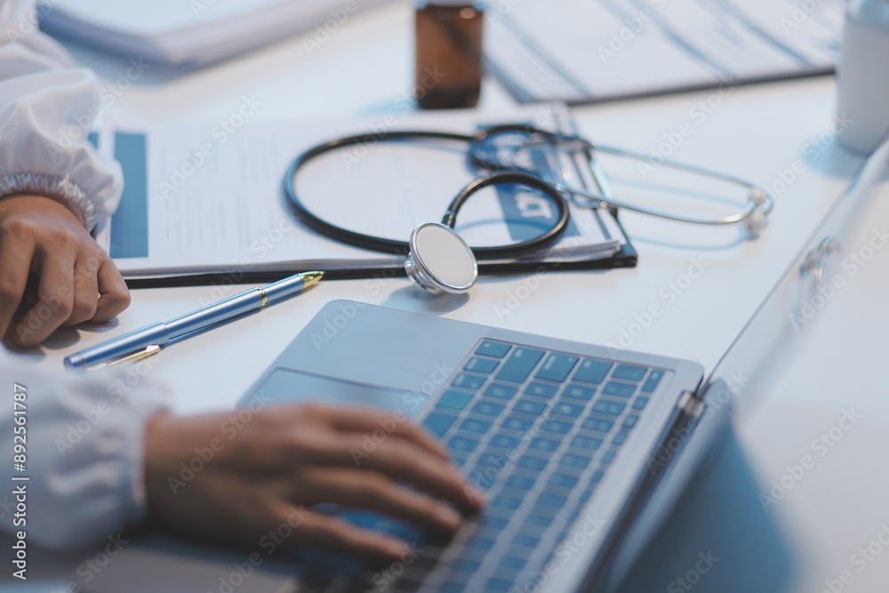 A professional and focused Asian female doctor in scrubs is working and reading medical research on her laptop in her office at a hospital. A professional and focused Asian female doctor in scrubs is working and reading medical research on her laptop in her office at a hospital.
