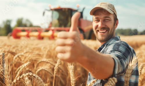 Farmer in a straw hat and plaid shirt stands in a field of wheat with a tractor in the background. He is giving a thumbs up and smiling directly at the camera