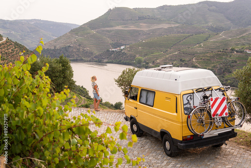 Blonde woman enjoying the view standing by her retro camper van parked in Douro valley. Summer time in Portugal