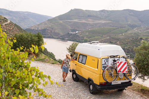 Blonde woman enjoying the view standing by her retro camper van parked in Douro valley. Summer time in Portugal