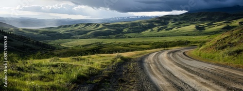  A dirt path winds through a lush green valley, framed by mountain ranges in the distance Overhead, clouds dot the expansive blue sky