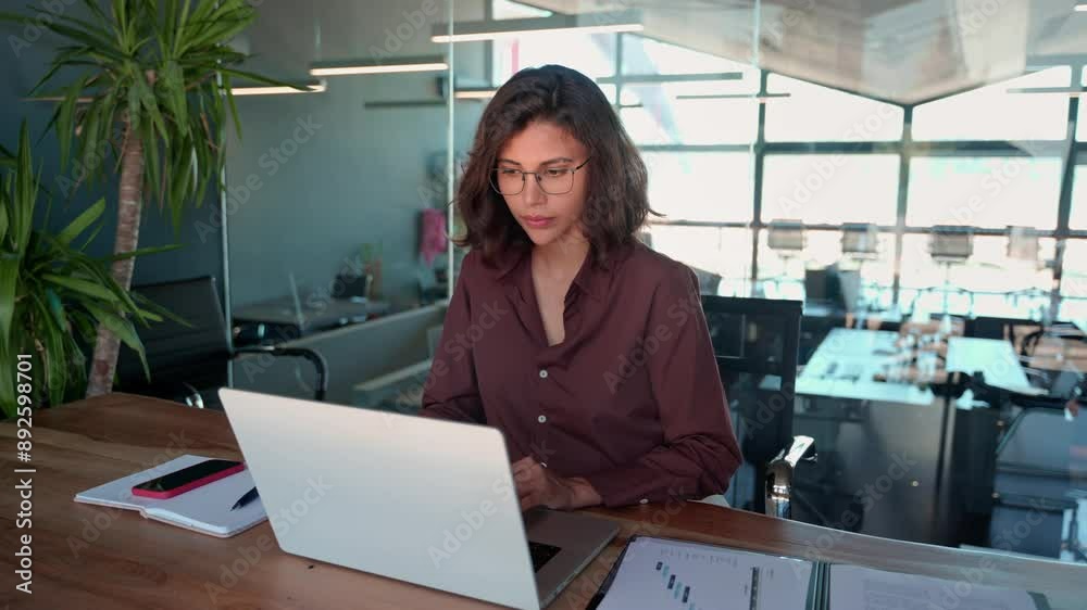 Smiling 30s latin hispanic middle-aged business woman working on laptop computer in modern office. Indian young businesswoman professional employee using pc doing online banking analysing at workplace