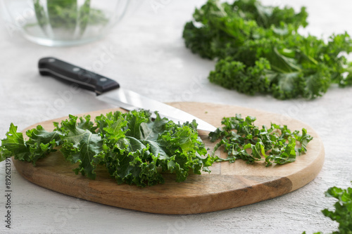 Wooden board of chopped curly kale on light gray textured background, vegan food, superfood. Cooking a delicious healthy salad