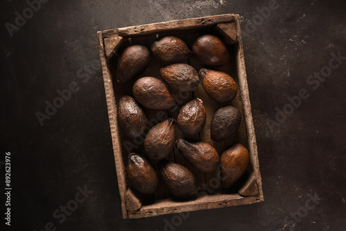 Top view of an old brown avocado in a wooden box on a black background in rustic style. The concept of aging, storage and spoilage of fruits, as well as a beautiful textured background. photo