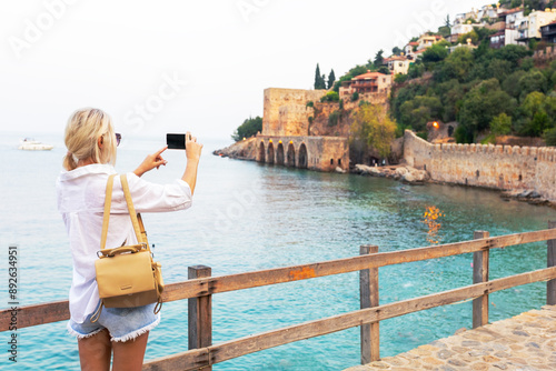 Traveller woman walking on the castle in Alanya and looking at the beautiful view at sunset.  tourist woman making photo or selfie with mobile phone, harbor of Alanya, Turkey.
