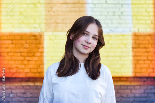 Portrait of perfect teen girl 13 year old with dimples in white jacket at colorful brick wall, smile looking at camera. Lovely teenager hipster lady on street. Youth gen z concept. Copy ad text space photo