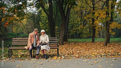 Elderly man and woman sitting on bench in amazing autumn park and reading letter together - dolly motion.