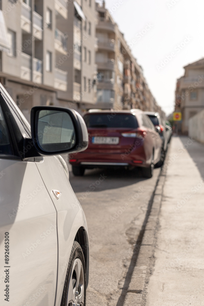 Fototapeta premium Line of parked cars along a narrow city street. Perfect for content related to urban transport, city living, automotive articles, or traffic management strategies. Parking price. Vertical picture.