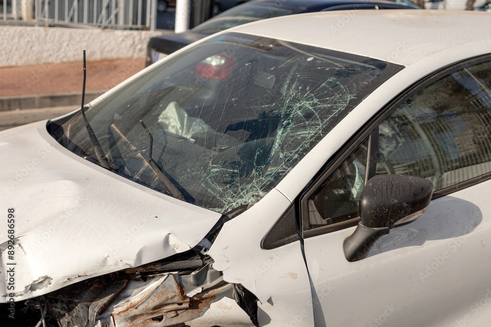 Obraz premium Close-up of car showing extensive front-end damage after collision, highlighting shattered windshield and deformed hood. Perfect for content on road safety, insurance claims, and automotive repairs.