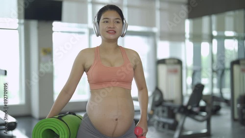 A portrait of happy Asian pregnant woman at gym fitness center club. Having a baby. Training workout. Exercise indoor with sport equipment. Athletic. Family people lifestyle. Mom love. Recreation.
