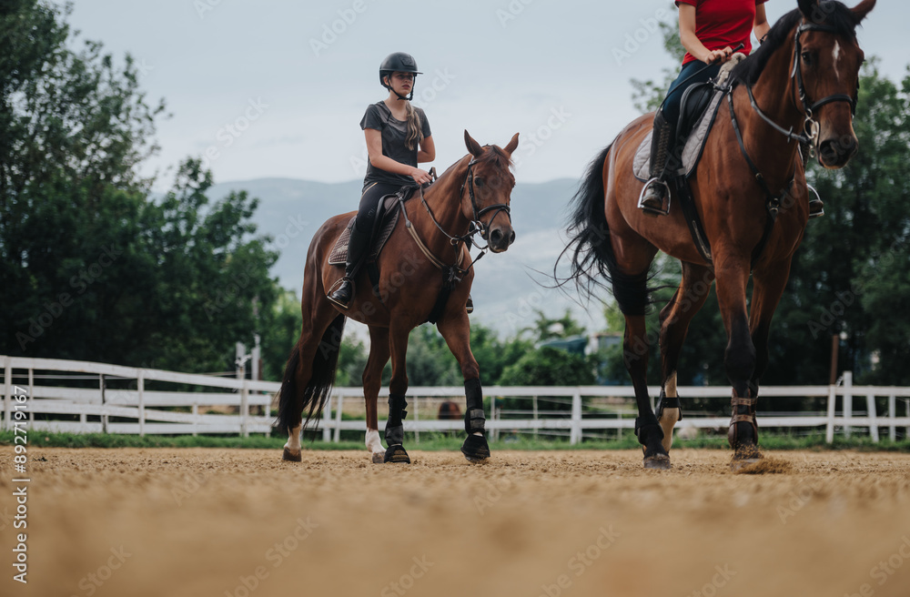 Two girls riding horses in an outdoor arena, showcasing equestrian skills and the bond between rider and horse on a cloudy day. Two girls riding horses in an outdoor arena, showcasing equestrian skills and the bond between rider and horse on a cloudy day.