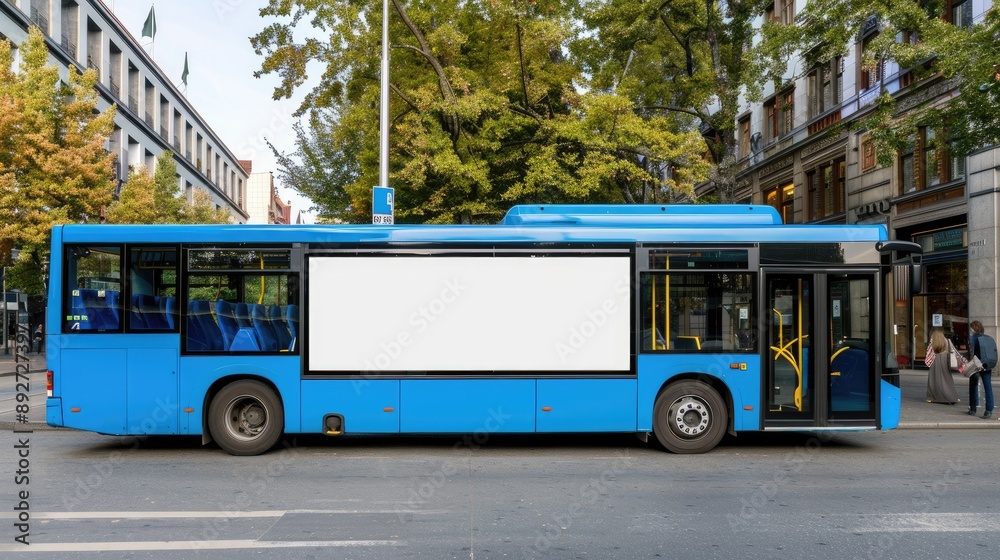 A blue tram travels down a city street, passing a bus stop with a blank billboard. A single person walks along the sidewalk A blue tram travels down a city street, passing a bus stop with a blank billboard. A single person walks along the sidewalk