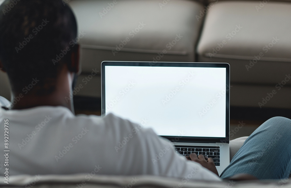 A man using a laptop with a blank screen while sitting on a sofa at home A man using a laptop with a blank screen while sitting on a sofa at home