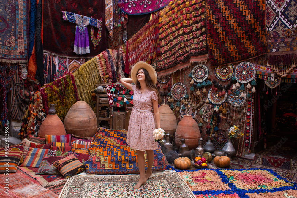 Fototapeta premium a beautiful girl in dress in a traditional turkish interior with many carpets on the wall