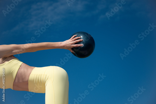 close up of a sporty woman holding a small pilates exercise ball outdoors. Wearing yellow sports clothing