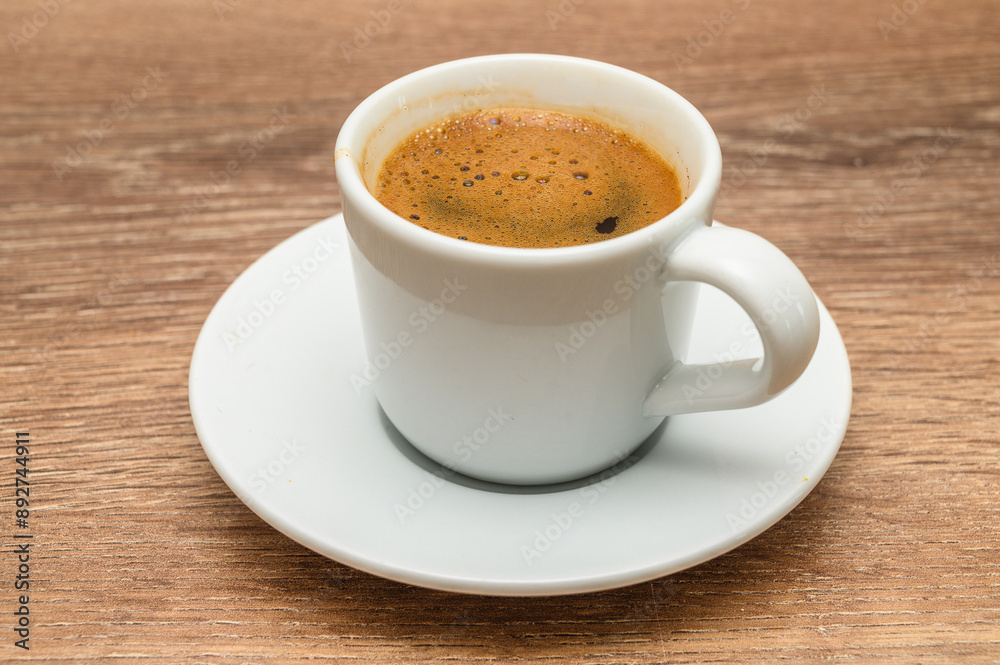 A coffee cup is elegantly placed on a saucer atop a wooden table A coffee cup is elegantly placed on a saucer atop a wooden table
