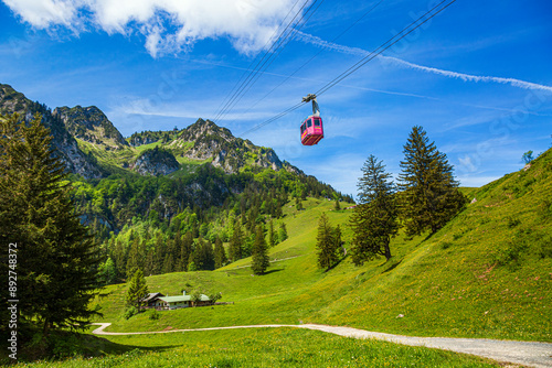 Die Hochfelln-Seilbahn fährt über grüne Wiesen und Tannenbäume vor einem Hintergrund aus beeindruckenden Bergen und blauem Himmel im Chiemgau, Bergen, Bayern, Deutschland photo