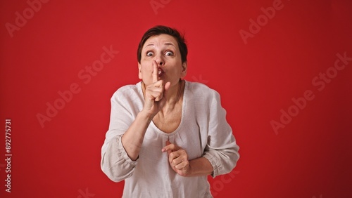Senior Woman Gesturing Silence on Red Background