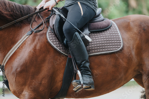 Detailed shot of a horseback rider's legs and saddle, highlighting the gear and equipment used in equestrian training and riding. photo