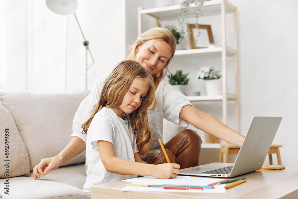 Mother and daughter bonding on the couch while learning and working together on a laptop in a cozy living room