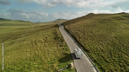 Aerial view of a campervan driving on a road through a beautiful mountain landscape. Drone slow motion shot tracking a motorhome on a highland road in a sunny evening