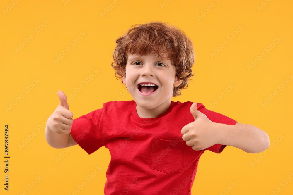 Portrait of happy little boy showing thumbs up on orange background Portrait of happy little boy showing thumbs up on orange background