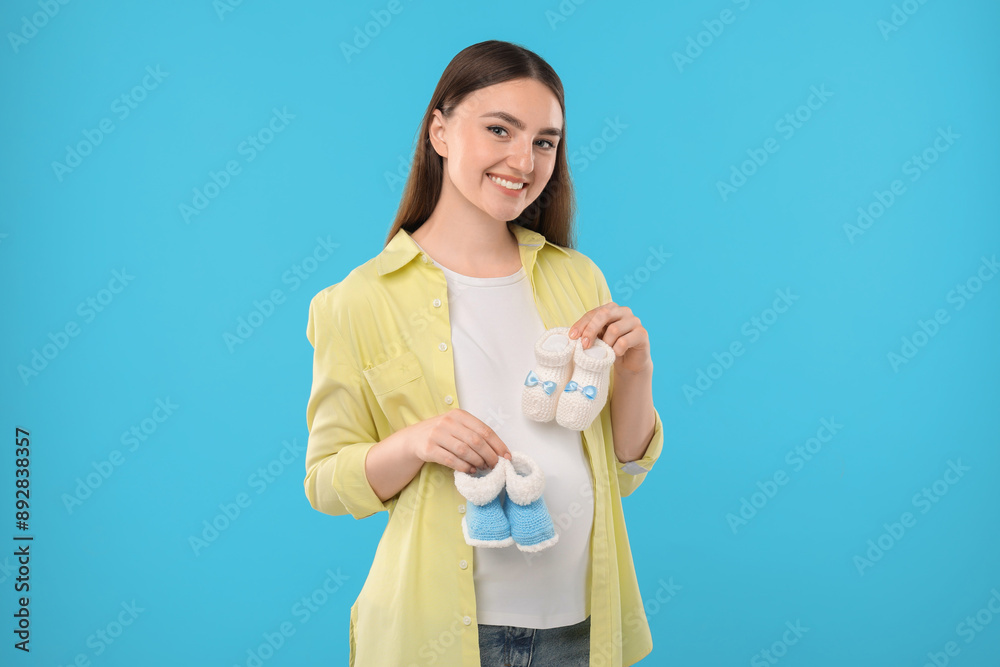 Expecting twins. Pregnant woman holding two pairs of baby shoes on light blue background Expecting twins. Pregnant woman holding two pairs of baby shoes on light blue background