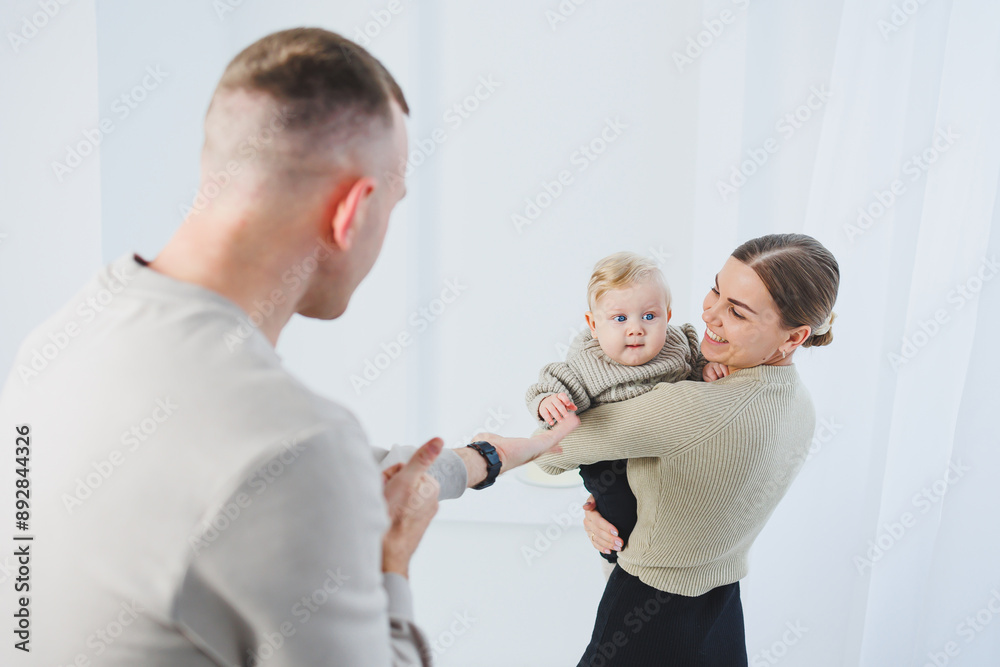 Obraz premium Young parents mom and dad are playing with a baby on a white background. A married couple hugs their newborn son. A happy family.