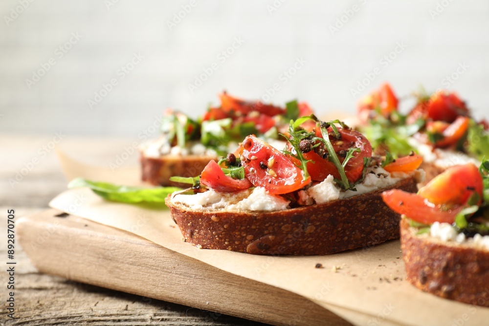Delicious ricotta bruschettas with tomatoes and arugula on wooden table, closeup