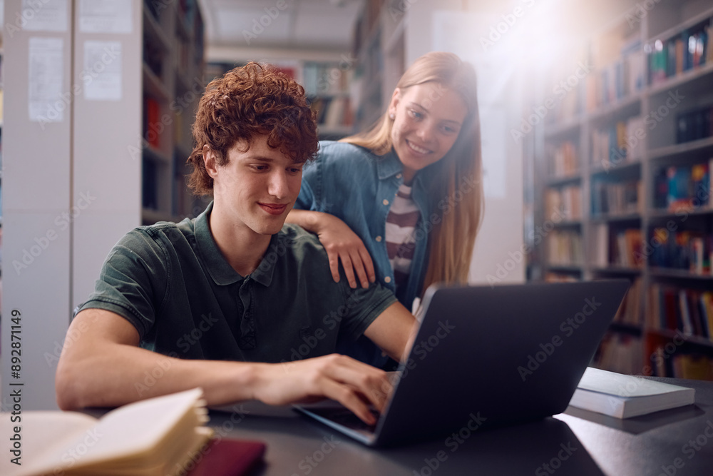 Happy college friends using laptop while studying in library. Happy college friends using laptop while studying in library.