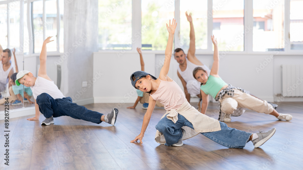 Fototapeta premium Concetrated preteen boys and girls studying movement of contemporary dance in classroom with his friends