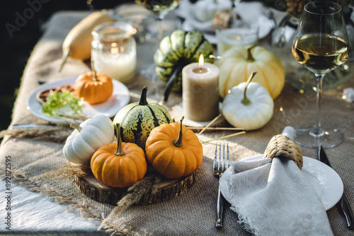 Cozy fall table decoration for Thanksgiving family dinner or romantic autumn wedding outdoors with small pumpkins, candles. White wine. Countryside style, cottage core, beautiful elegant setting photo