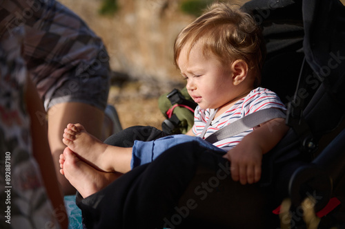 Fotografie Toddler sitting calmly in a stroller during a sunny outdoor activity, enjoying t