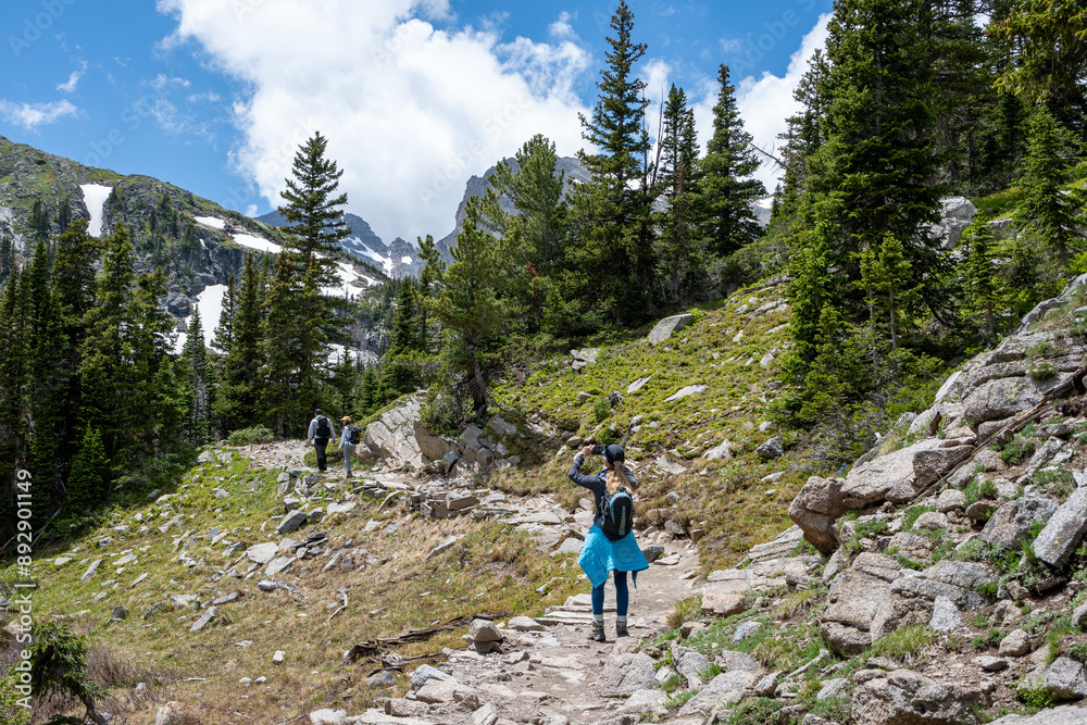Three hikers on Lake Isabelle Trail in Brainard Lake Recreation Area, Colorado. under towering mountains and sunny summer cloudscape. Three hikers on Lake Isabelle Trail in Brainard Lake Recreation Area, Colorado. under towering mountains and sunny summer cloudscape.