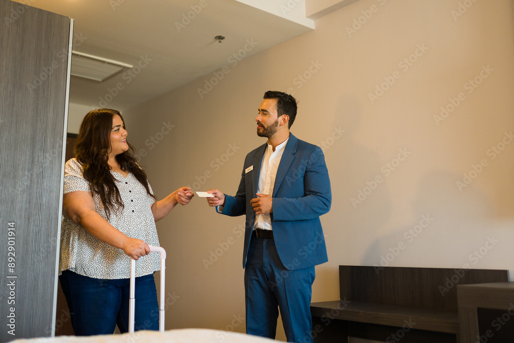 Fototapeta premium Hotel manager presents room key card to female guest with luggage, smiling warmly