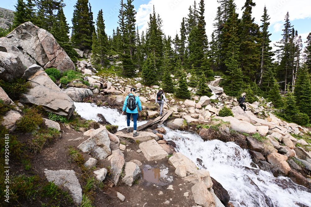 Φωτογραφία Three hikers crossing stream on narrow log bridge on Lake Isabelle Trail in Brainard Lake Recreation Area, Colorado on sunny summer afternoon