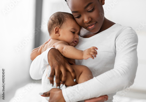 Maternity Concept. Portrait of young African American mother hugging and holding her upset crying baby on hands. Displeased hungry infant whining, feeling pain or colic. Copy space, blurred background