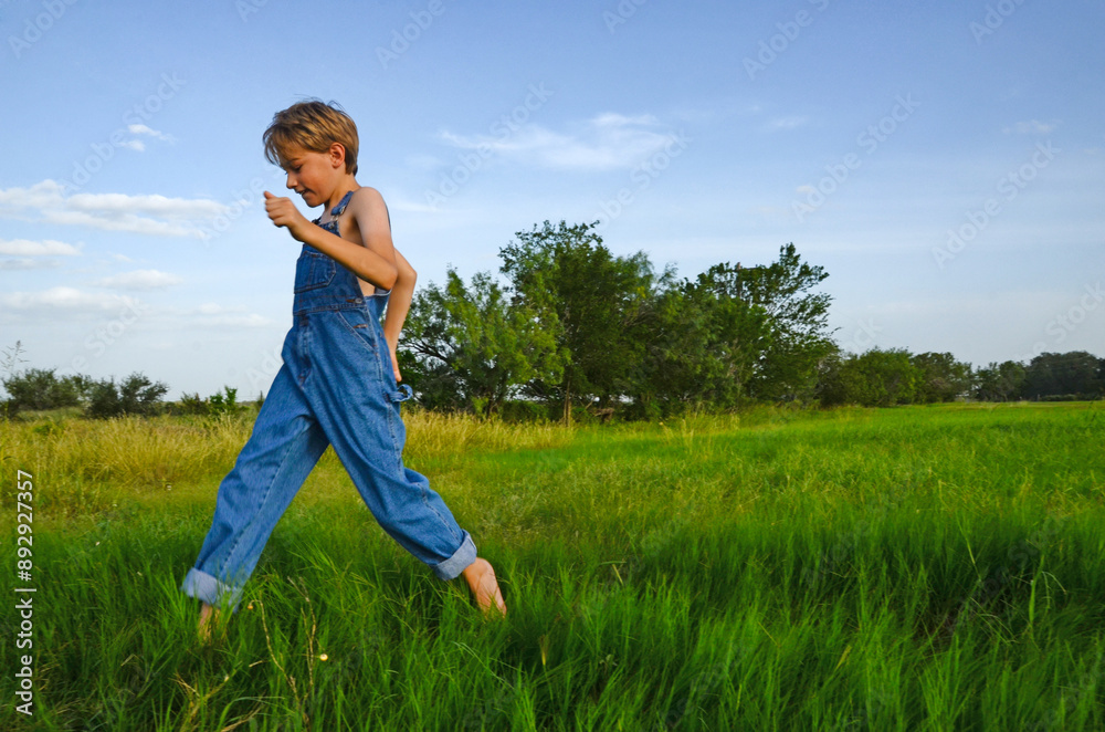 Summertime springtime young preteen boy running through green grass wearing overalls Summertime springtime young preteen boy running through green grass wearing overalls