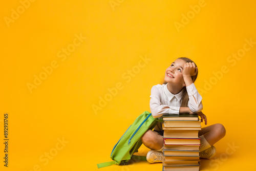 Ready For School. Adorable Little Girl Dreaming Sitting With Backpack At Stack Of Books On Yellow Background. Copy Space
