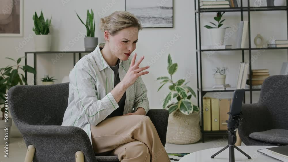 Medium side shot of happy deaf Caucasian girl answering video call on smartphone, greeting and waving hello to friend, chatting using sign language hand gestures, while relaxing at home Medium side shot of happy deaf Caucasian girl answering video call on smartphone, greeting and waving hello to friend, chatting using sign language hand gestures, while relaxing at home