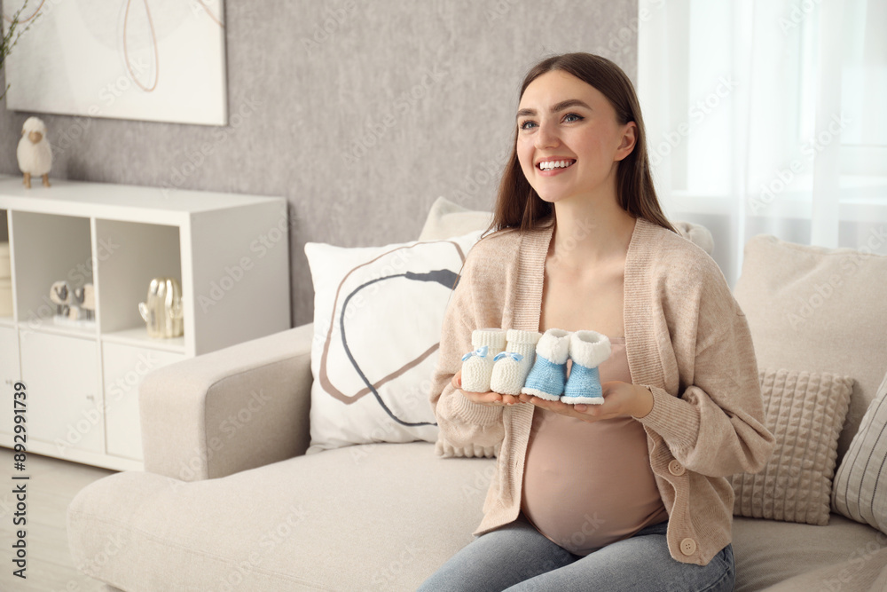 Expecting twins. Pregnant woman holding two pairs of shoes at home, space for text