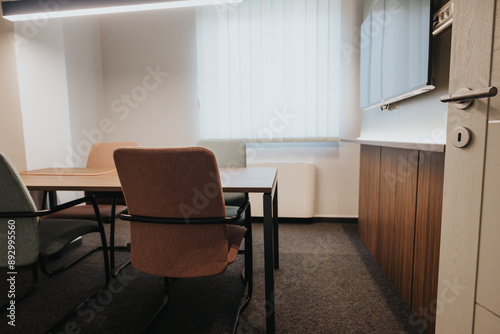 A contemporary office meeting room featuring stylish chairs, a wooden table, and minimalist decor under bright lighting.