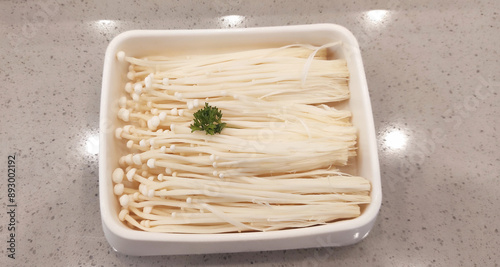 Enoki mushrooms are food mushrooms with long, white cultivated fruit bodies like bean sprouts. Served in a white bowl for food as suki which is boiled hot. Isolated on dotted gray marble background photo